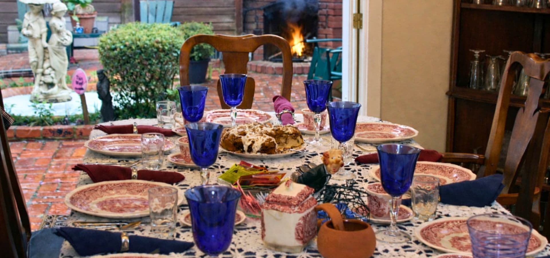 A beautifully set dining table with blue glasses and decorative plates, overlooking a garden and a fireplace.