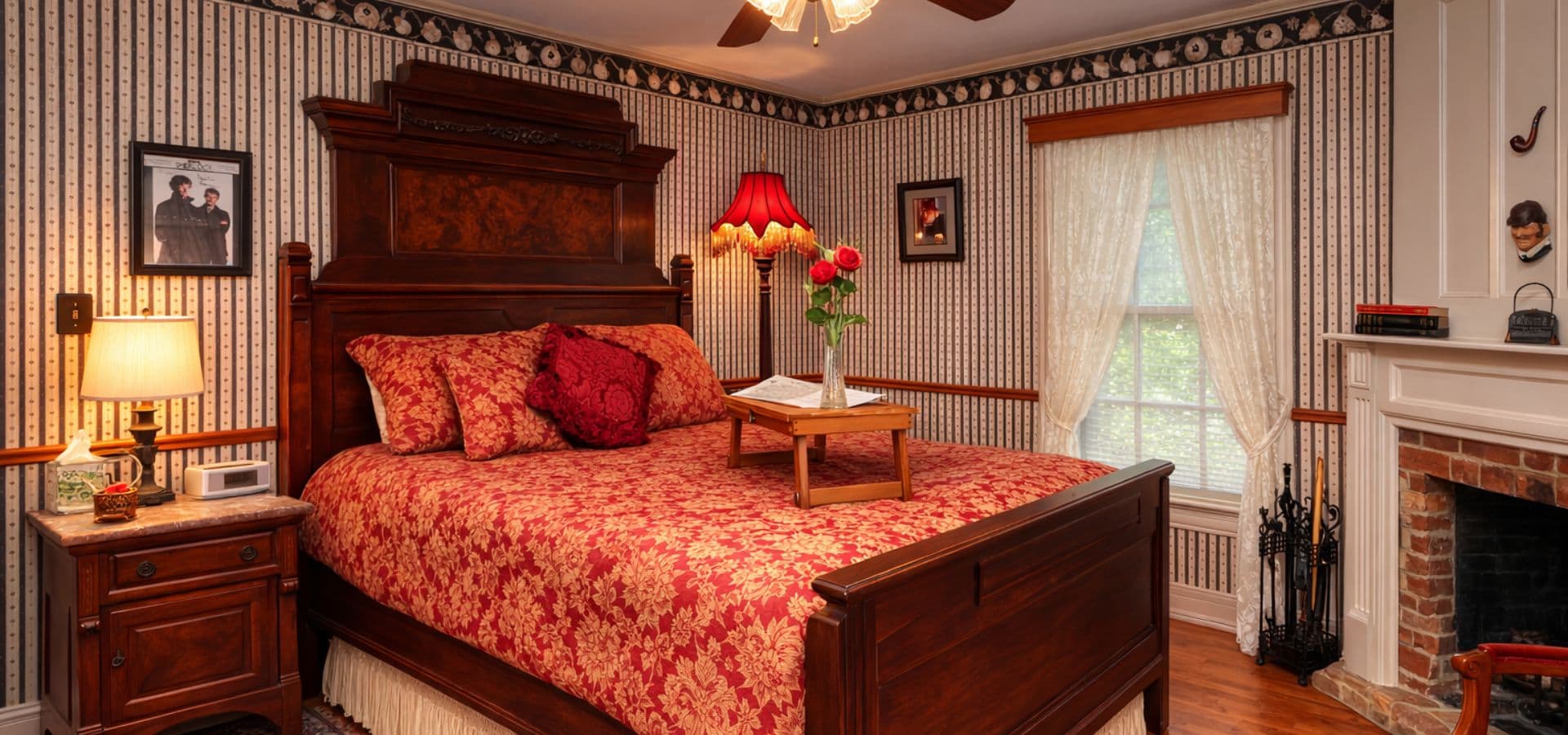 A cozy bedroom featuring a wooden bed with a floral quilt, bedside table, and a window with sheer curtains.