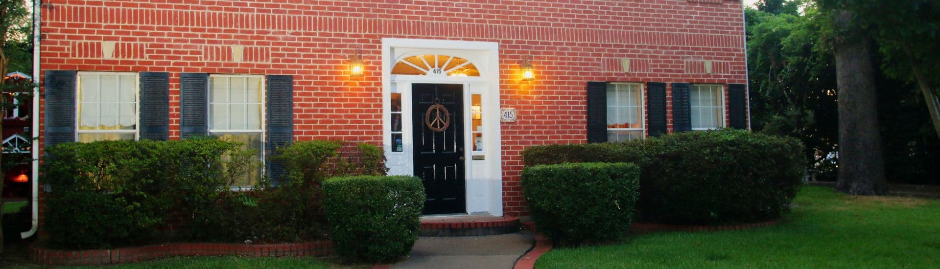 A brick house with a black front door, surrounded by neat shrubs and lawn.