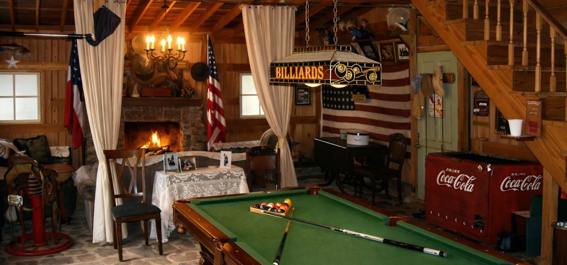 A cozy rustic game room with a pool table, fireplace, and American flags decorating the walls.