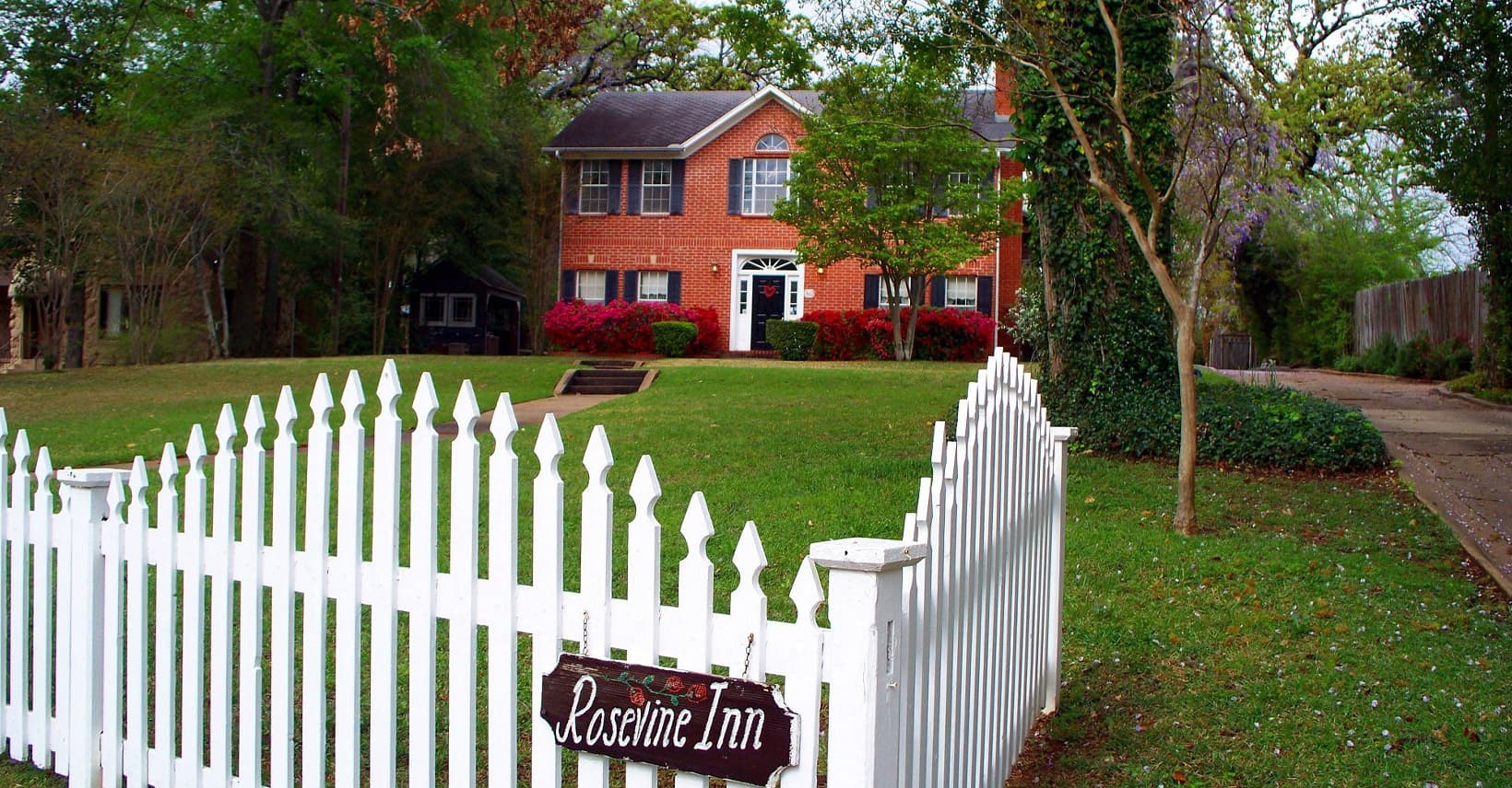Large red brick home with expansive lawn behind a white picket fence Large red brick home with expansive lawn behind a white picket fence