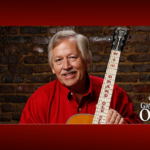 photo of John Conlee in a red shirt holding a guitar