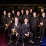 Photo of the group of twelve musicians with their instruments. They all have black on and they are called Beatles to Bourbon