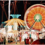 Scene of a fair with rides lit up and people walking looking at vendors booths