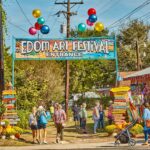 overhead sign says Edom Arts Festival leads into the grounds. many people going in. Colorful balloons above the sign.