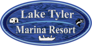 Blue oval sign with the words Lake Tyler Marina Resort in grey lettering clip art of camper, fish and a boat also on the sign